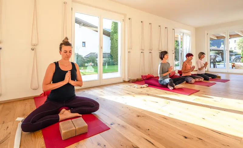 Gemeinsame Meditation im hellen yogamood Studio: Yogalehrerin im Vordergrund, dahinter Teilnehmerinnen auf Yogamatten